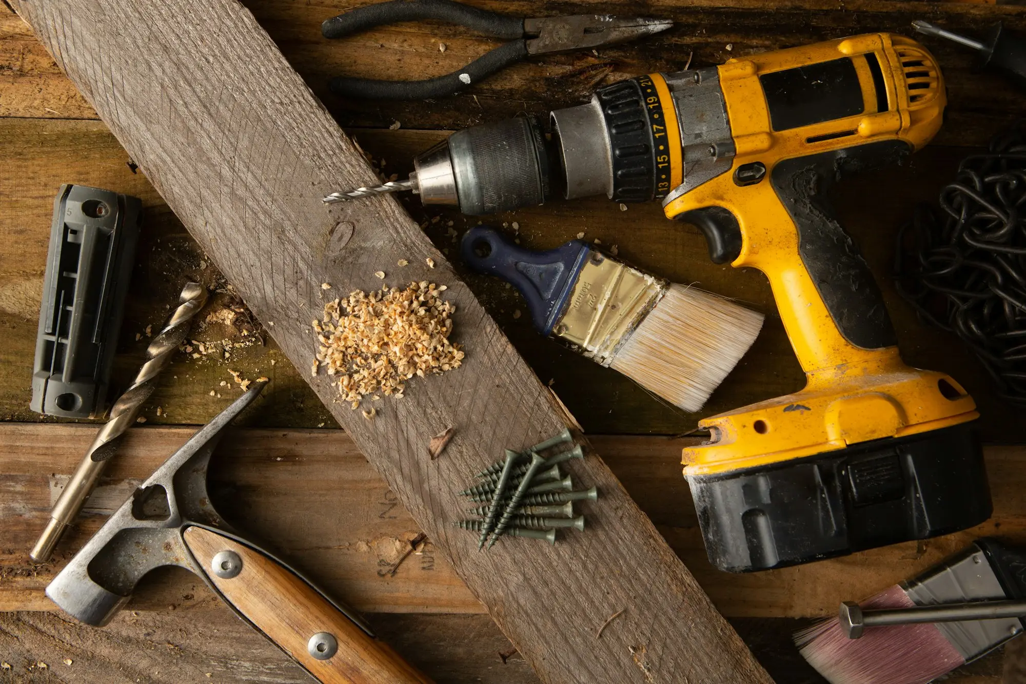Cordless drill, claw hammer, paintbrush and screws on a timber plank, the working tools of a builder who runs a small company and pays themselves from it