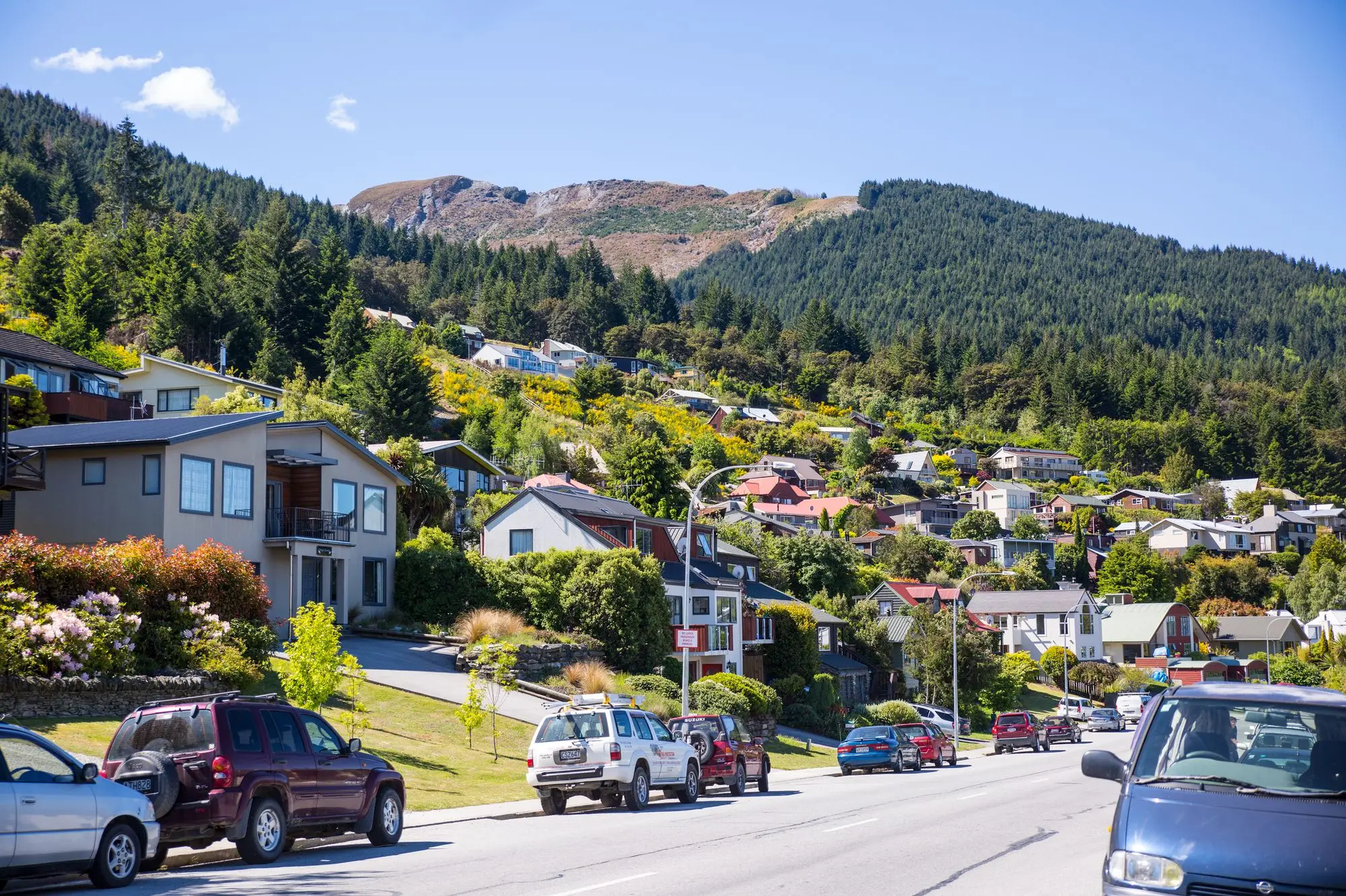 Hillside street of family homes and townhouses in Queenstown, New Zealand, with cars parked along the kerb
