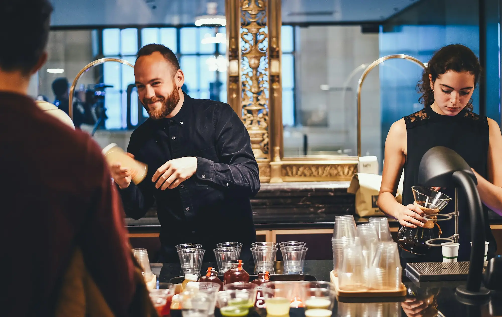 Two hospitality business partners working side by side behind a bar counter preparing drinks